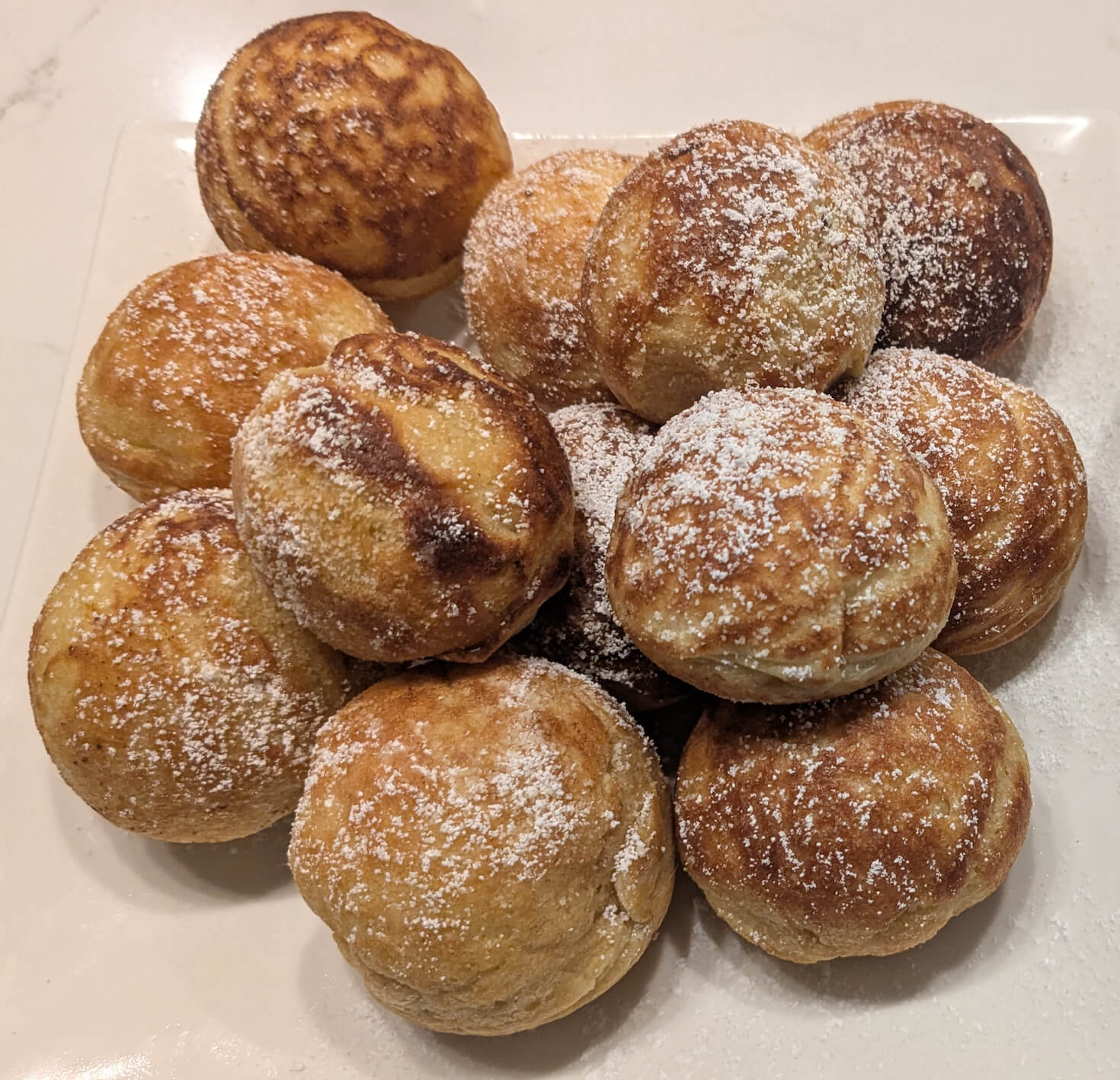 Freshly made Danish æbleskiver on a plate, dusted with powdered sugar