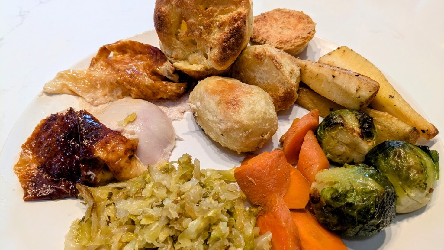 British roast dinner with chicken, roast potatoes, brussels sprouts, yorksire pudding, carrots, and parsnips