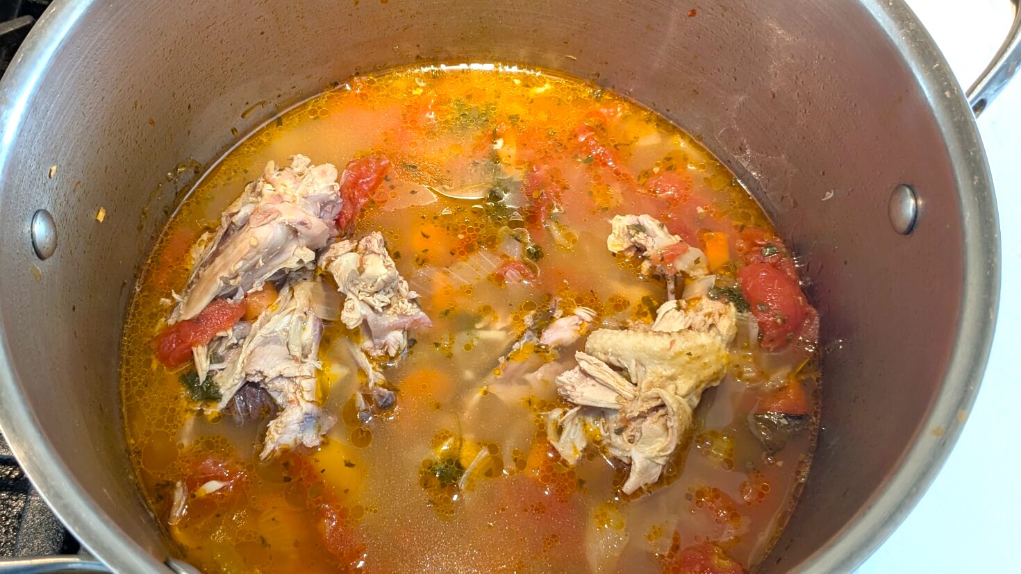 Italian chicken soup cooking in a pot with orzo, tomato, and herbs