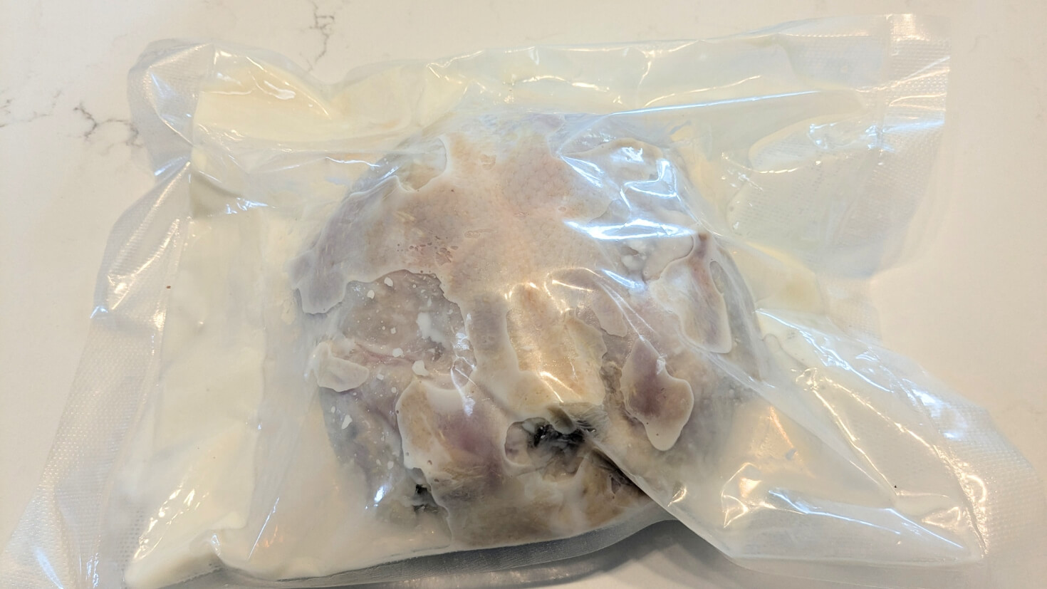 Whole chicken marinating in salted buttermilk and garlic in a vacuum-sealed bag